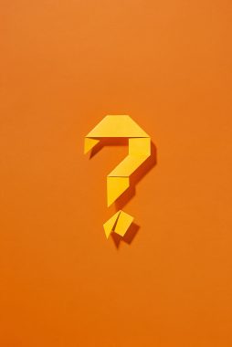 Colorful yellow origami question mark with shadow centered on orange background in a creative conceptual image with copy space